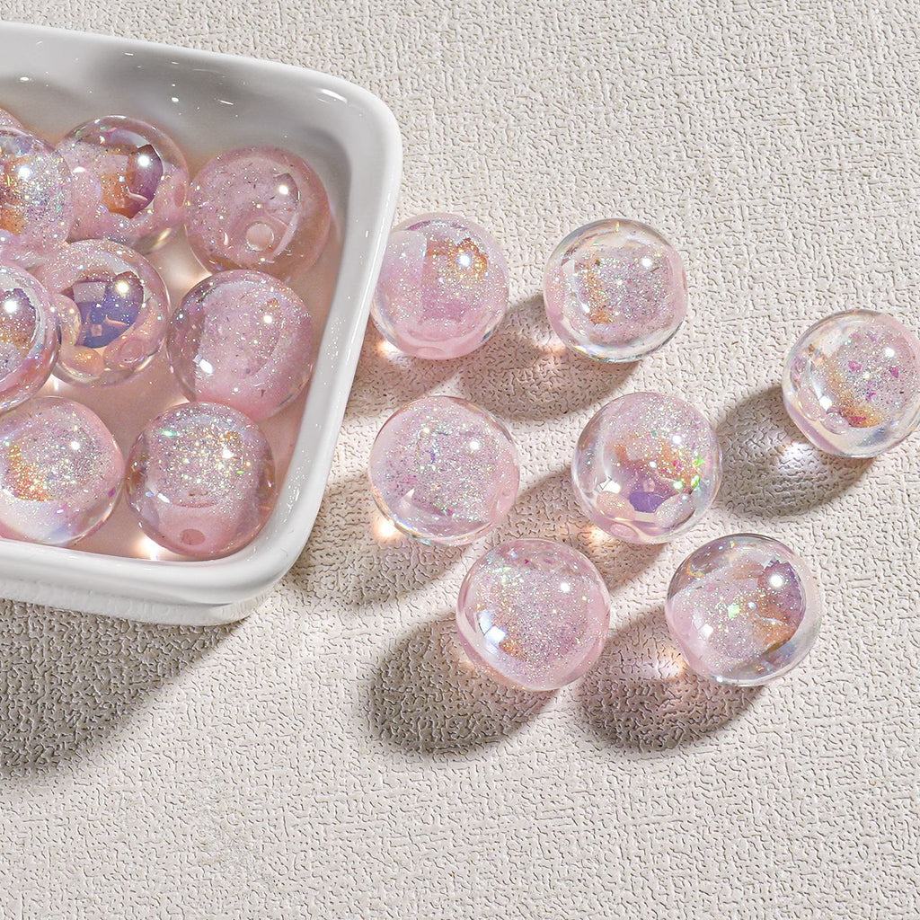 Clear round candy-core opal-effect resin beads filled with pink glitter and iridescent flecks in white dish