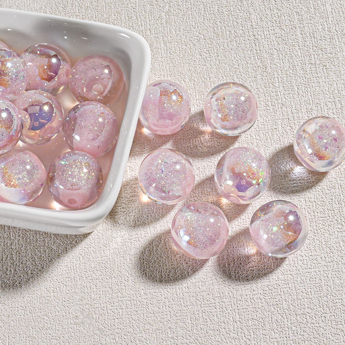 Clear round candy-core opal-effect resin beads filled with pink glitter and iridescent flecks in white dish