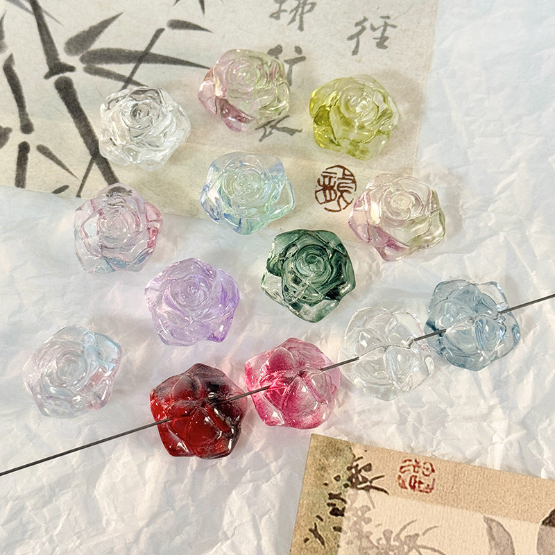 Translucent rose-shaped glass beads in pink, red, green, blue, purple and clear arranged on a textured white surface