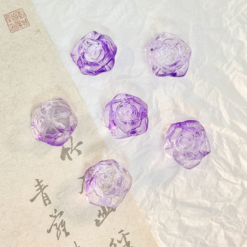 Five purple translucent rose-shaped beads arranged on a split background of textured beige paper and white crumpled paper.
