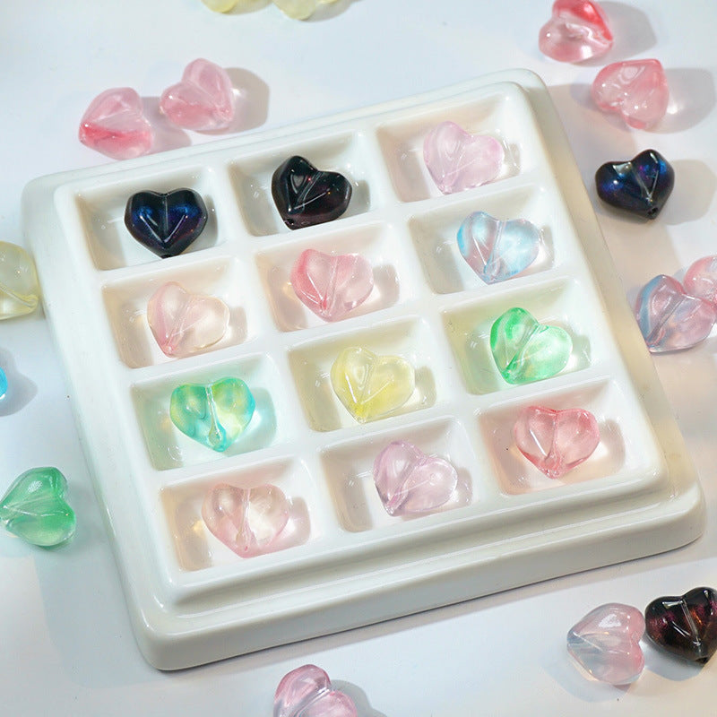 Translucent heart-shaped glass beads in pastel and dark colors arranged in a white compartment tray