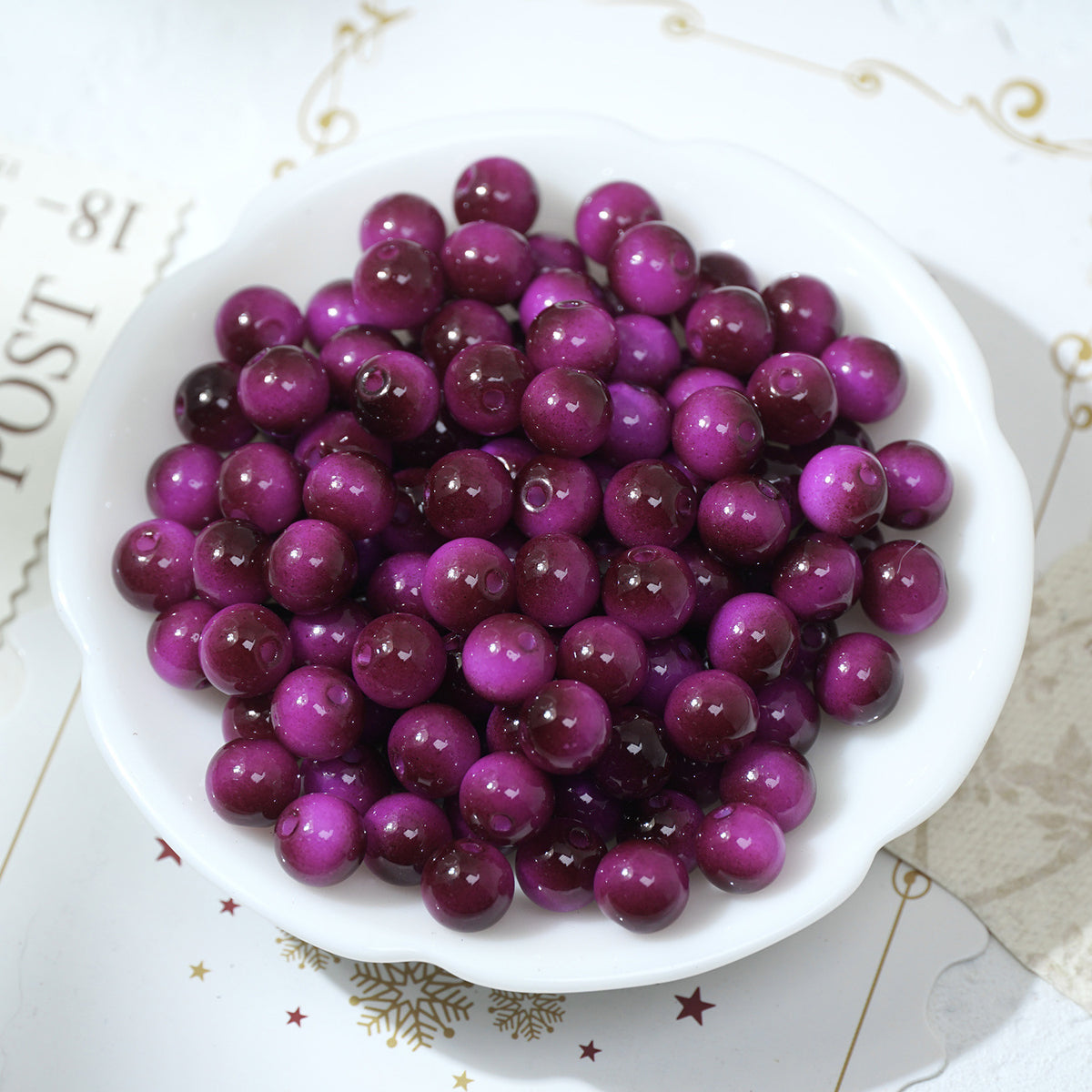 Glossy round purple and magenta glass beads in a white scalloped bowl