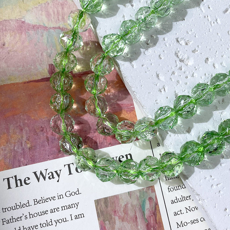 Strand of faceted light green glass beads draped over an open book page on a textured white surface
