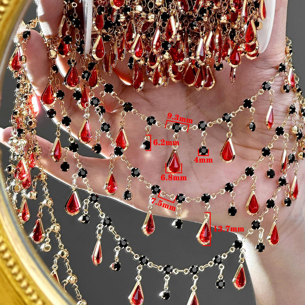 A gold-tone chain choker necklace with red teardrop crystals and black faceted beads, draped over a hand with red dimension labels showing measurements.
