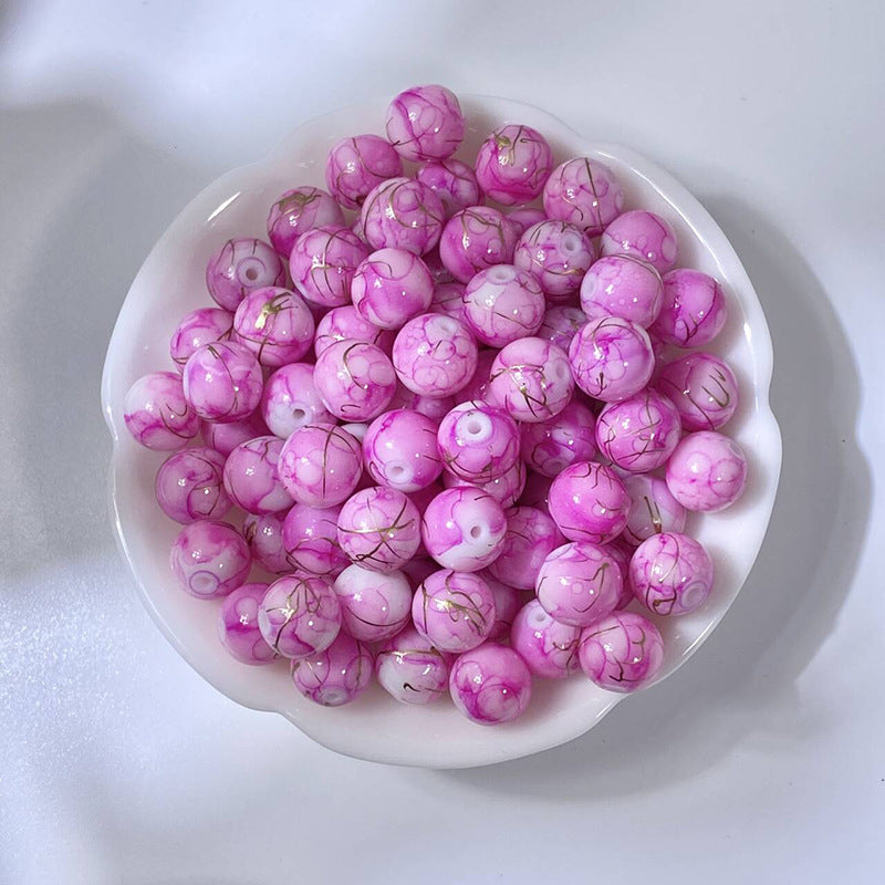 White bowl of marbled magenta-pink glass beads with gold-silk veining
