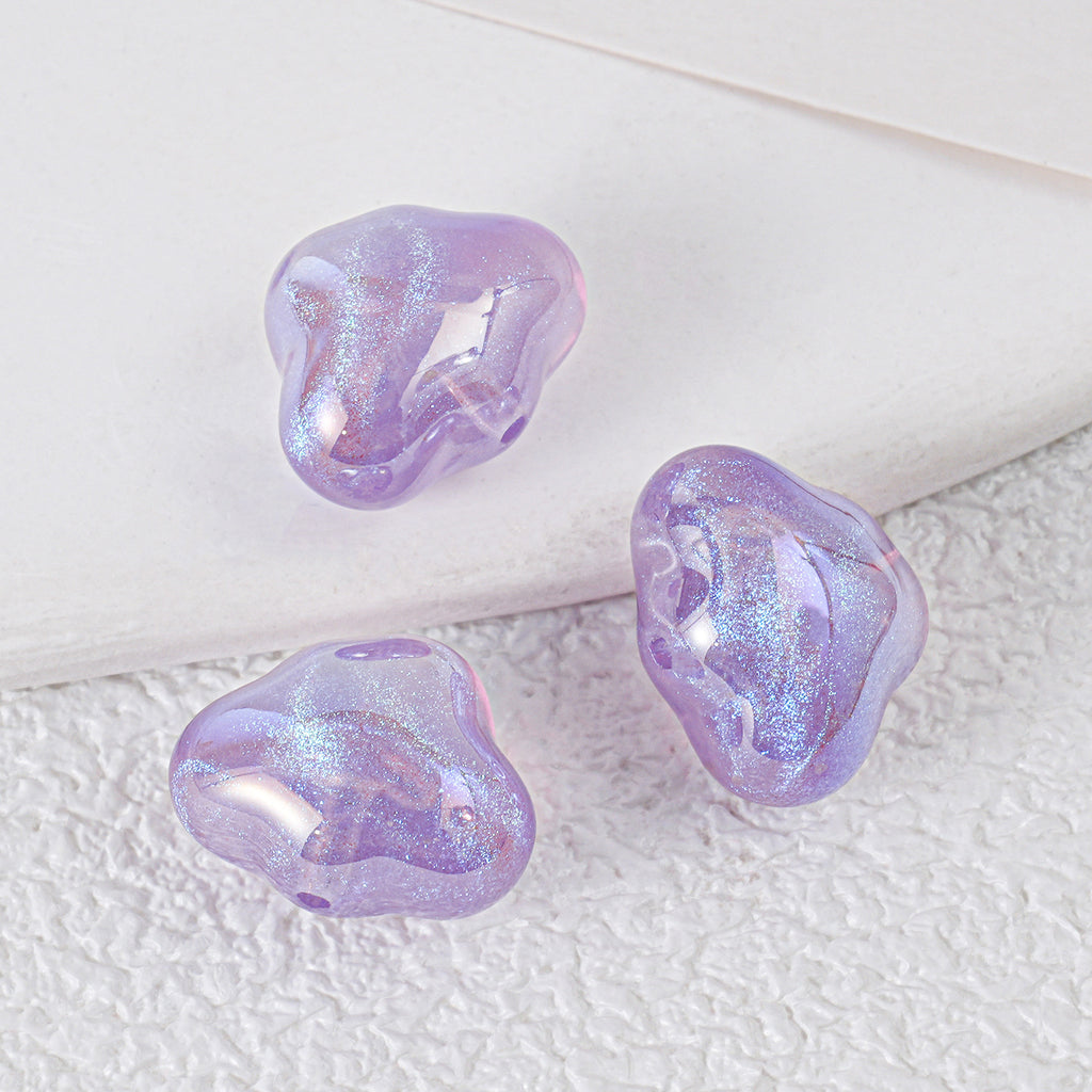 Three iridescent lavender-purple cloud-shaped resin beads with shimmering finish on a textured white surface