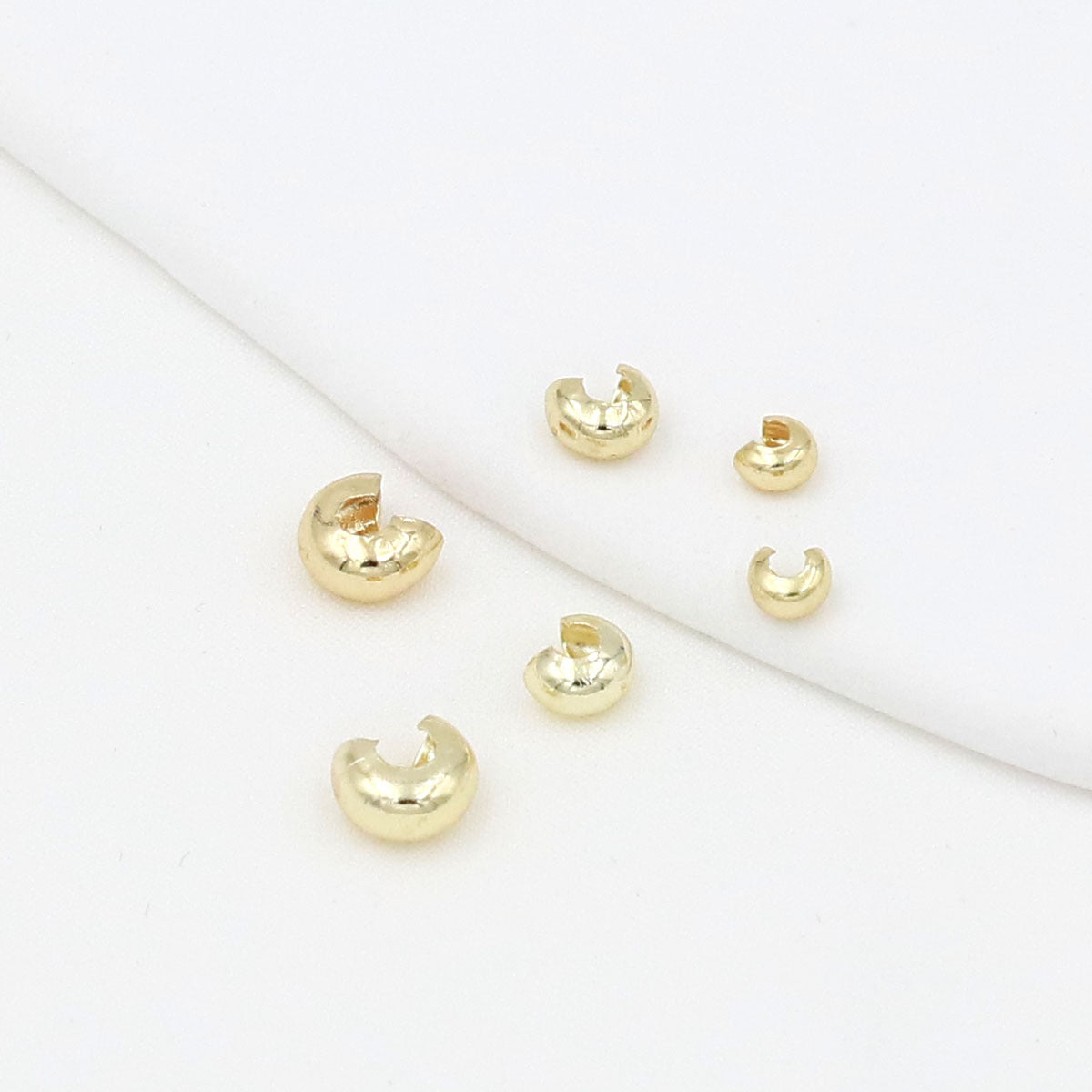Six small gold C-shaped crimp bead covers scattered on a white background