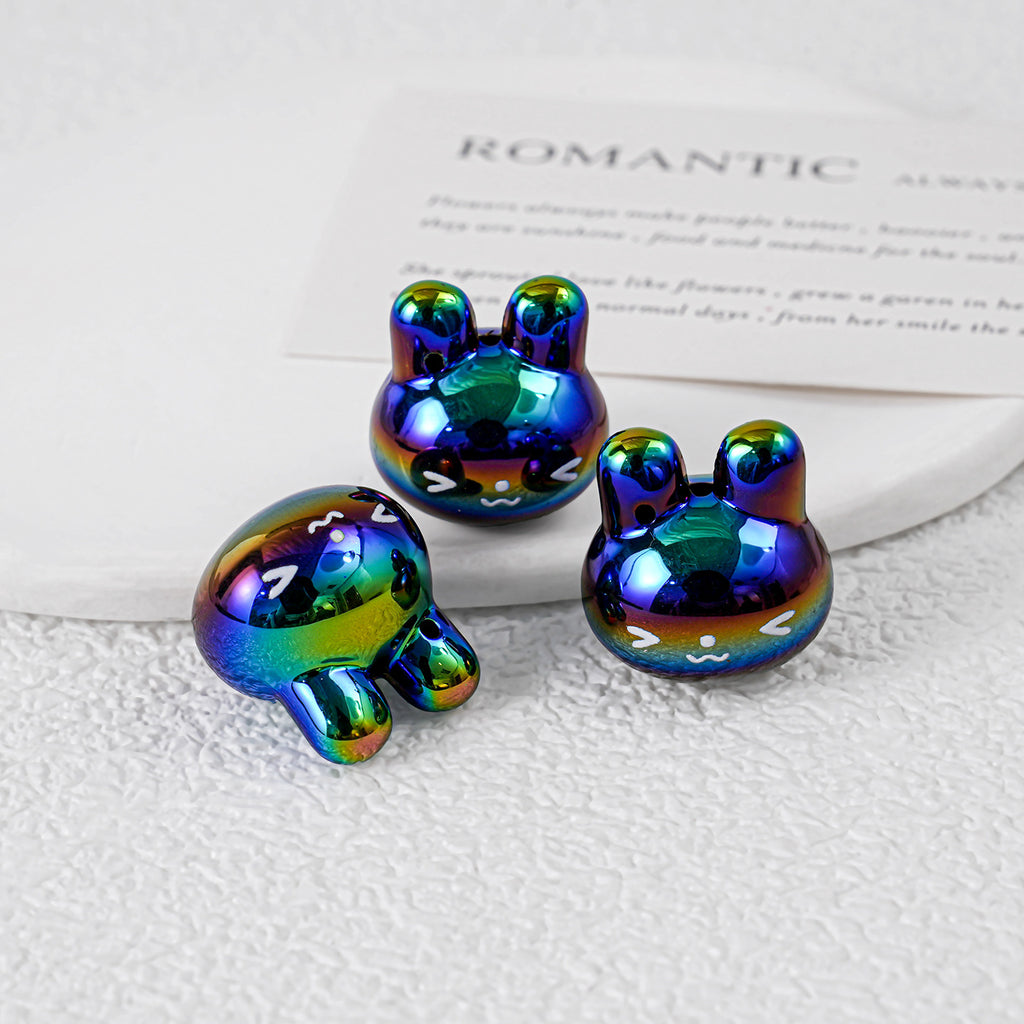 Three iridescent rainbow bunny-shaped acrylic charms on white textured surface