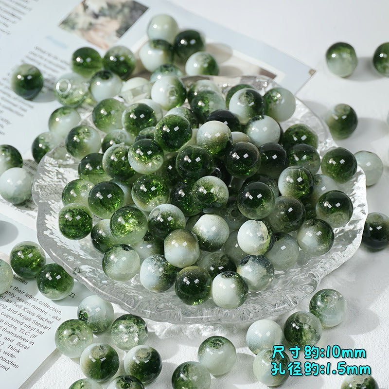 Green and white ice-crackle glass beads piled in a clear textured glass bowl with scattered beads