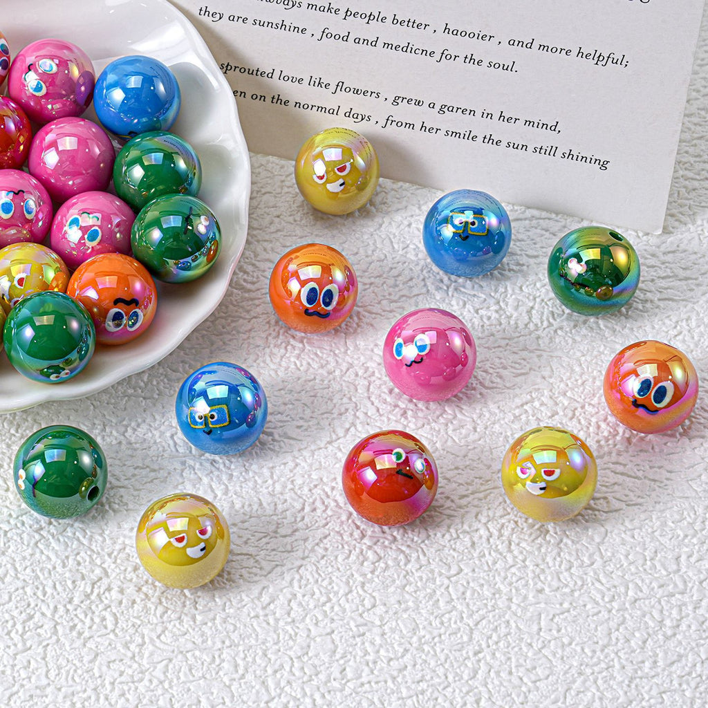 Colorful iridescent resin round beads with cartoon faces, in white bowl and scattered on textured fabric with printed card