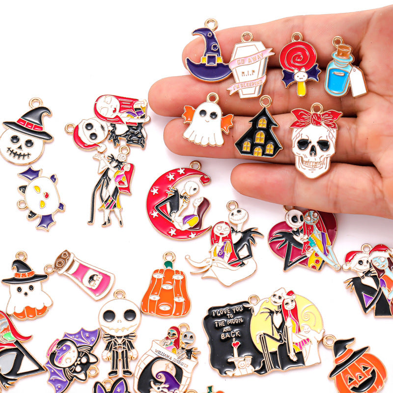 Hand holding colorful enamel Halloween alloy charms, witch hats, ghost, skull, haunted house, more scattered on white.