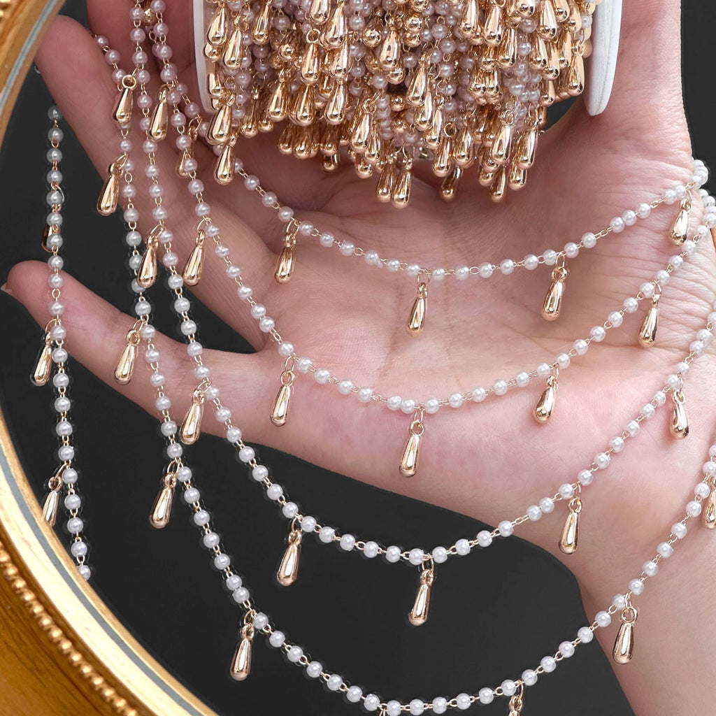 Hand holding layered faux pearl chains with rose gold teardrop charms against a dark background