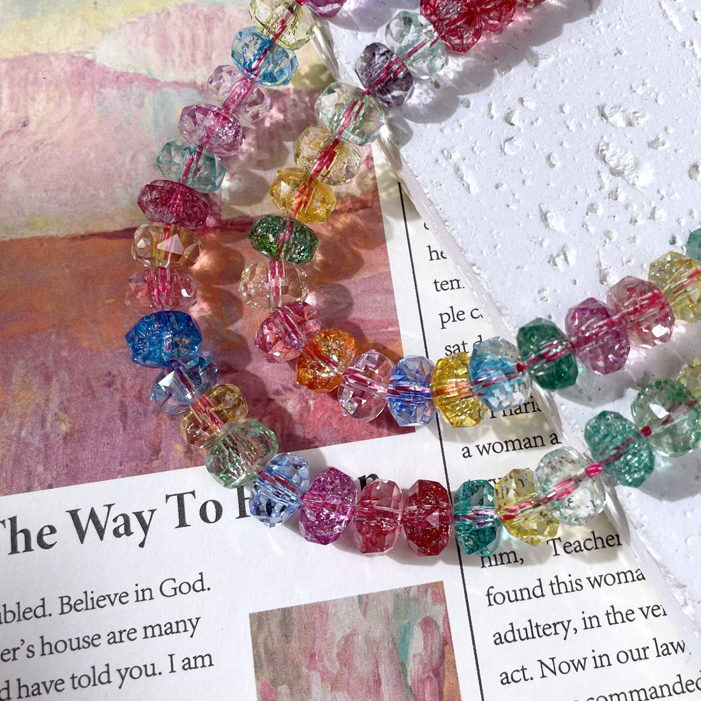 A close-up of a beaded strand with faceted, rainbow-colored beads arranged on a printed paper background.
