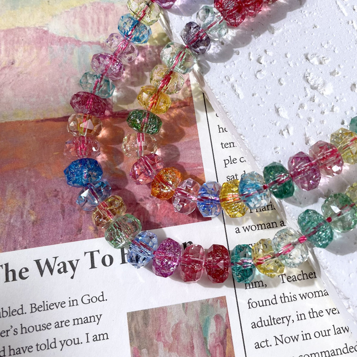 A close-up of a beaded strand with faceted, rainbow-colored beads arranged on a printed paper background.