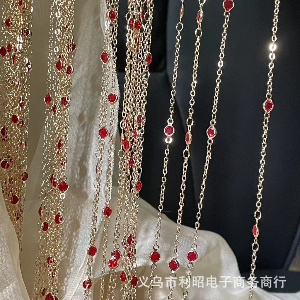 A decorative hanging curtain made of multiple gold-tone chains adorned with small red faceted beads, draped over a white fabric backdrop against a dark background.