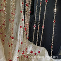 A decorative hanging curtain made of multiple gold-tone chains adorned with small red faceted beads, draped over a white fabric backdrop against a dark background.