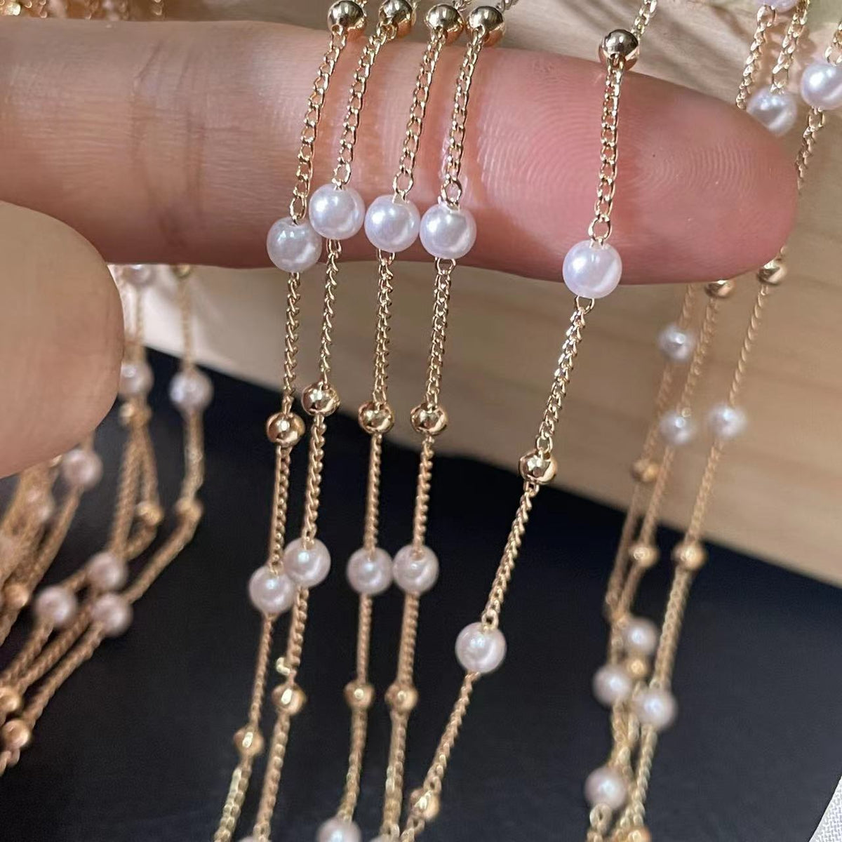 Gold-toned multi-strand chains with white pearl beads held across a person's fingers