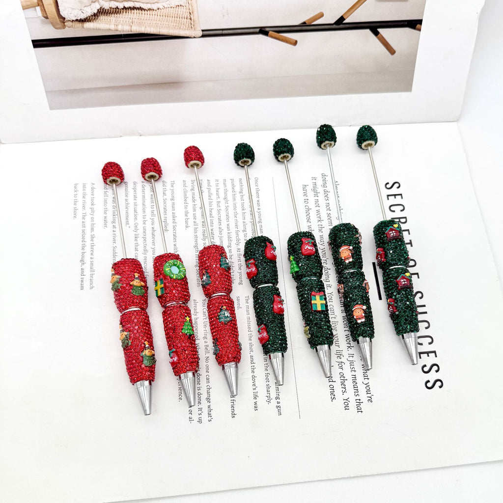 Six rhinestone ballpoint pens with Christmas cartoon designs on an open book.