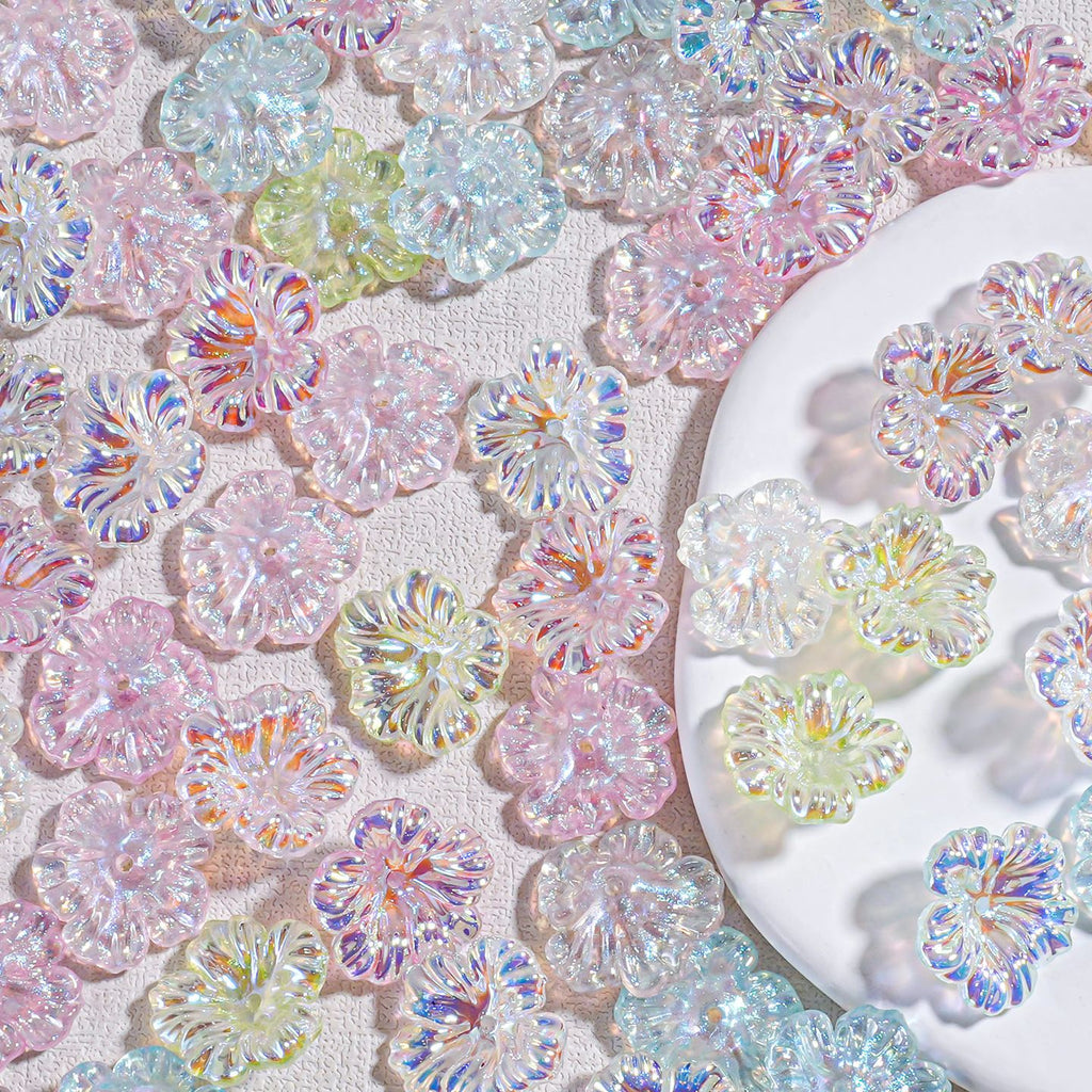 Iridescent resin hibiscus flower beads in pastel pink, blue and green scattered on white fabric