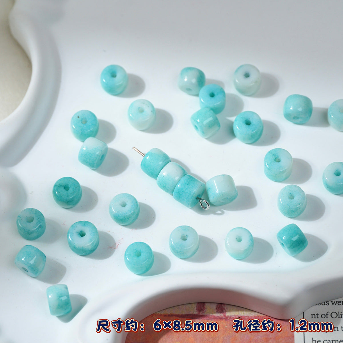 Light blue-green round porcelain seed beads on white, one strand threaded
