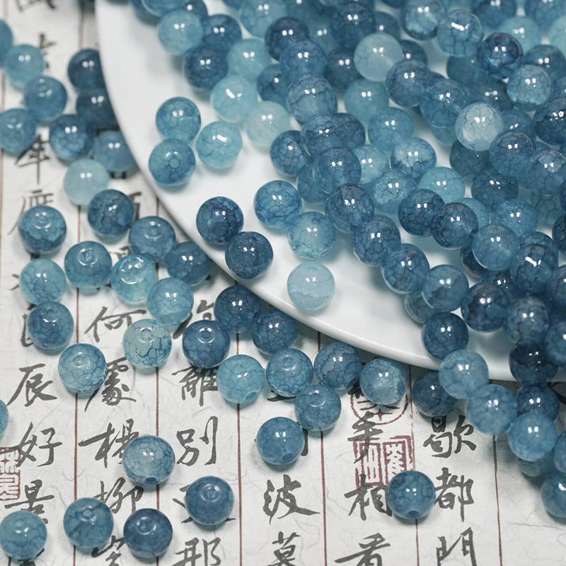 Sea blue ice-crackle glass beads spilling from a white plate onto calligraphy paper