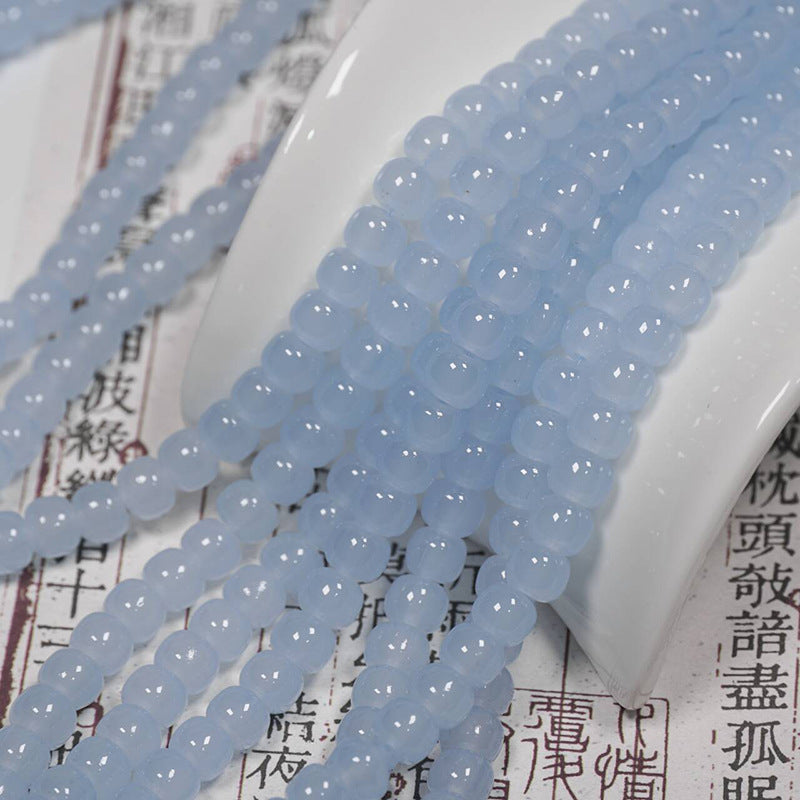 Light blue translucent round beads arranged in strands over a white ceramic spoon and printed paper background.