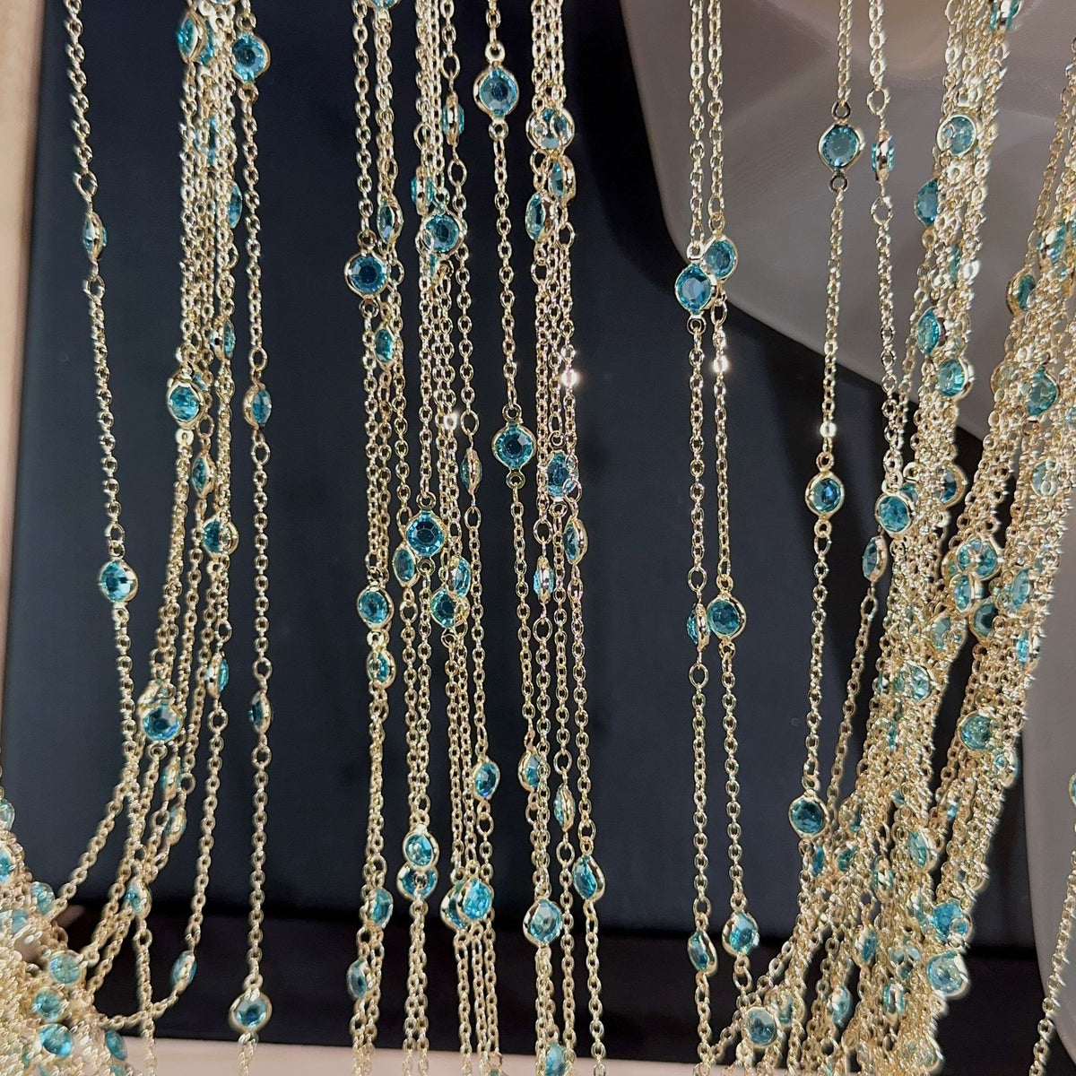 Close-up of gold-toned multi-strand necklace with dangling chains, turquoise-blue beads