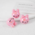Three glossy pink bunny-shaped acrylic beads with black faces on white textured surface