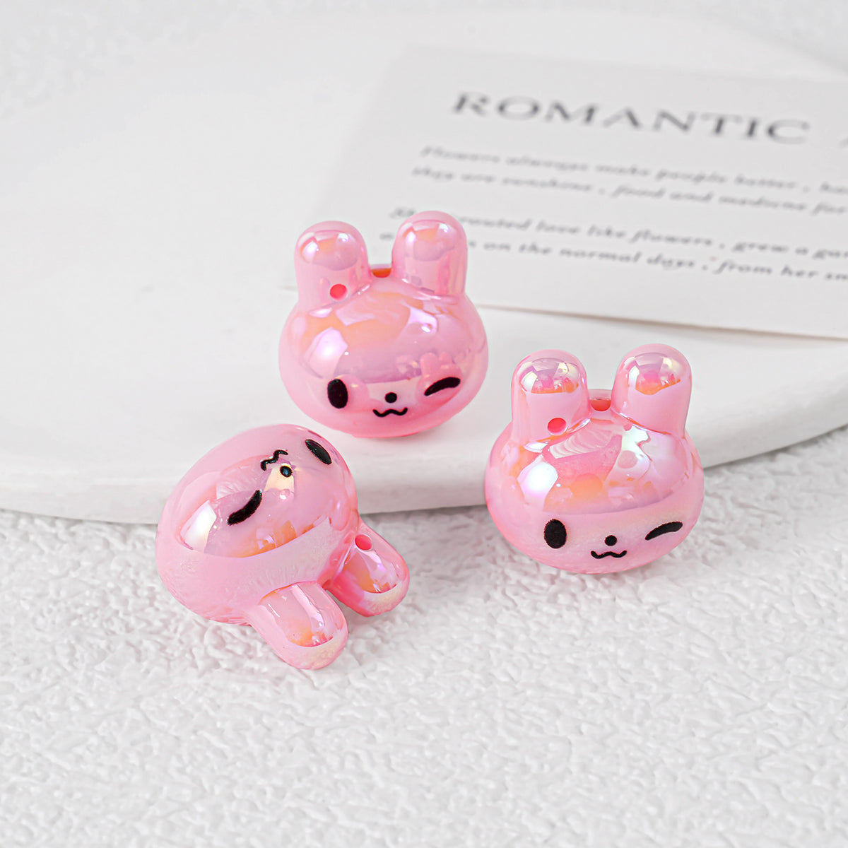 Three glossy pink bunny-shaped acrylic beads with black faces on white textured surface