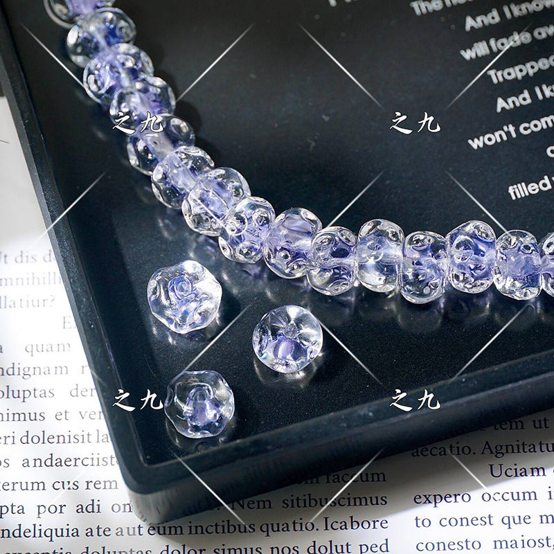 Clear faceted lampwork beads with lavender-purple centers on a black tray, loose beads