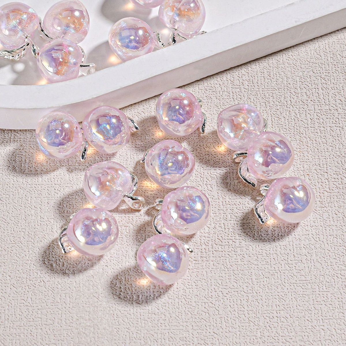 Iridescent pink heart-shaped mini peach beads with silver wire loops on a textured beige surface
