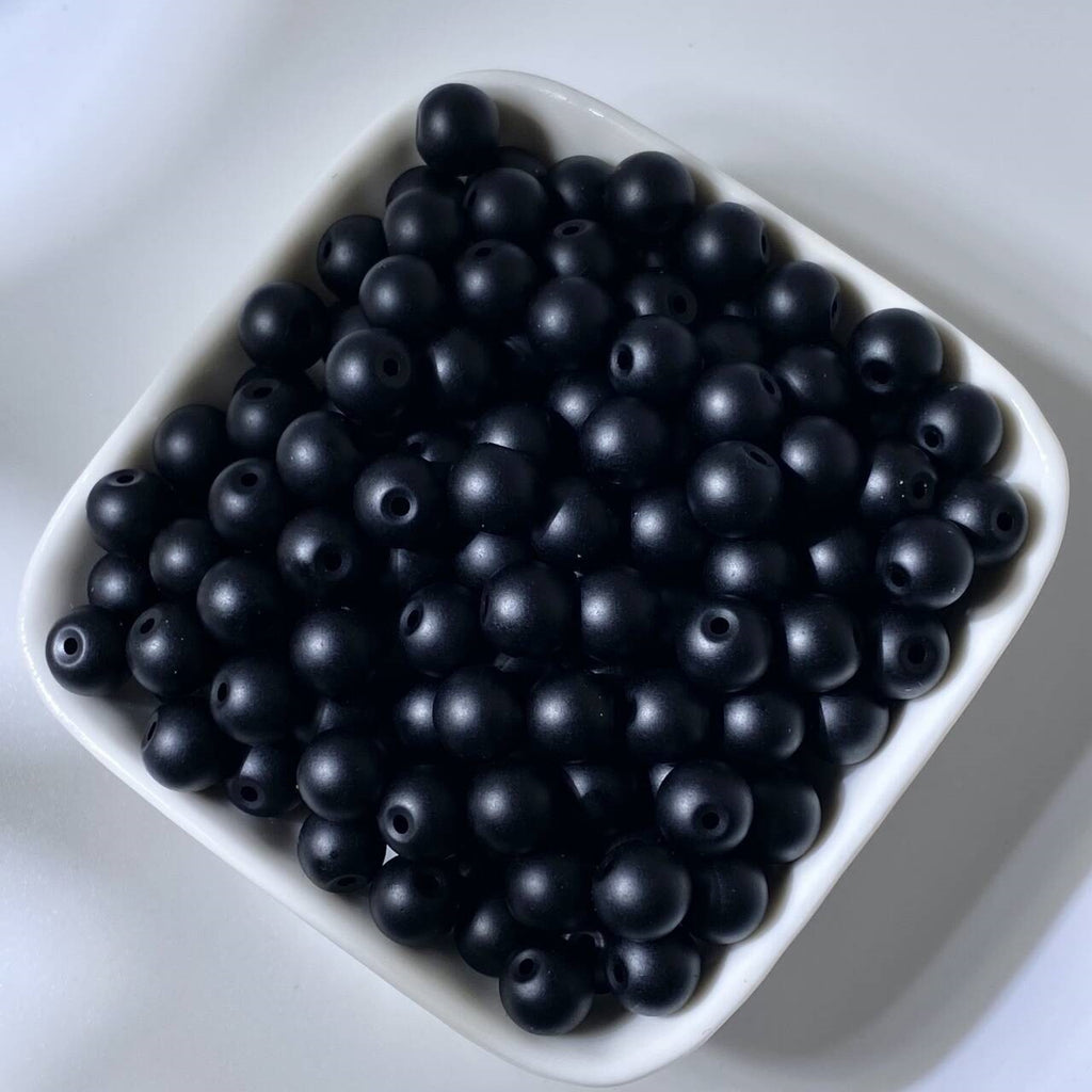 Matte black round beads in a white square bowl on white background