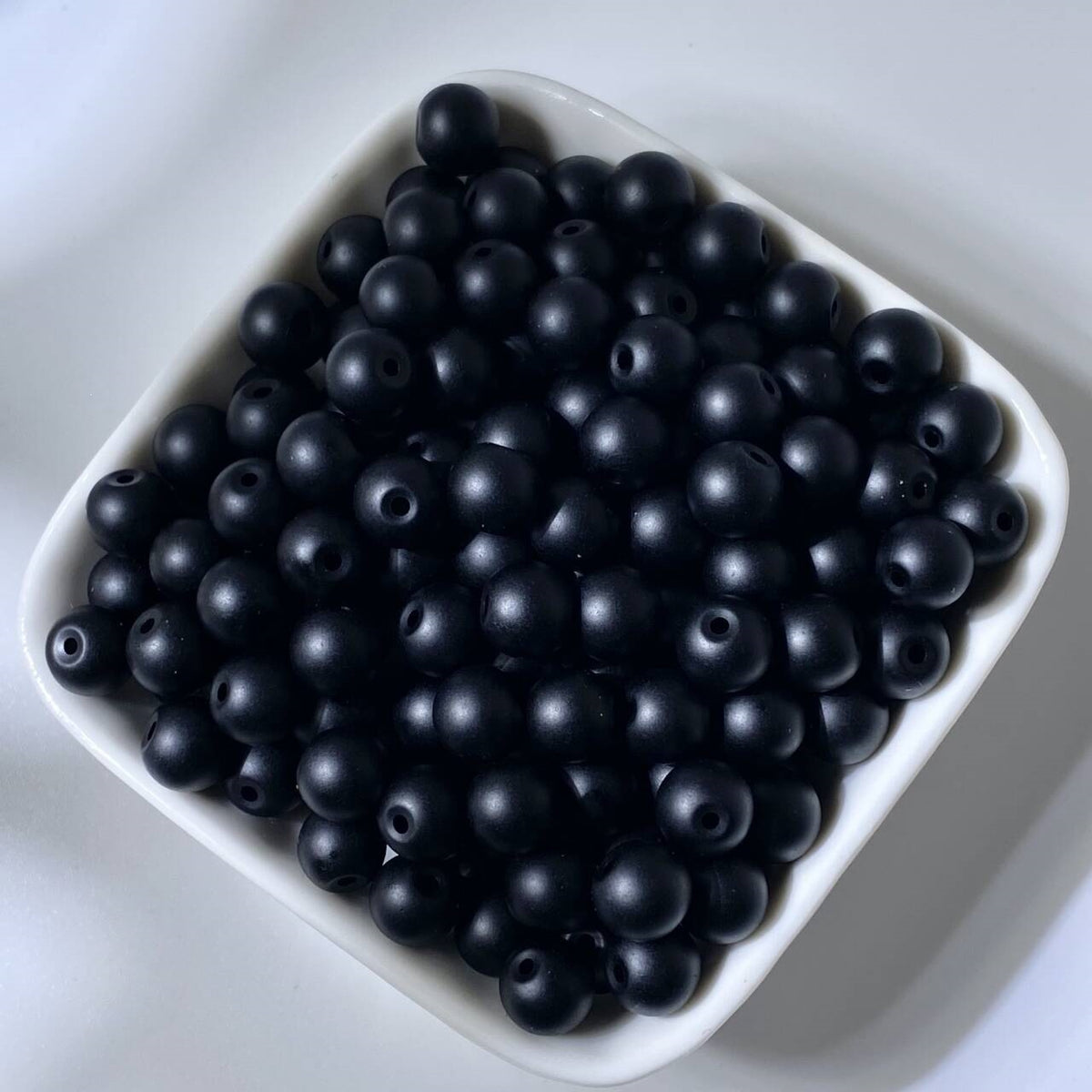 Matte black round beads in a white square bowl on white background