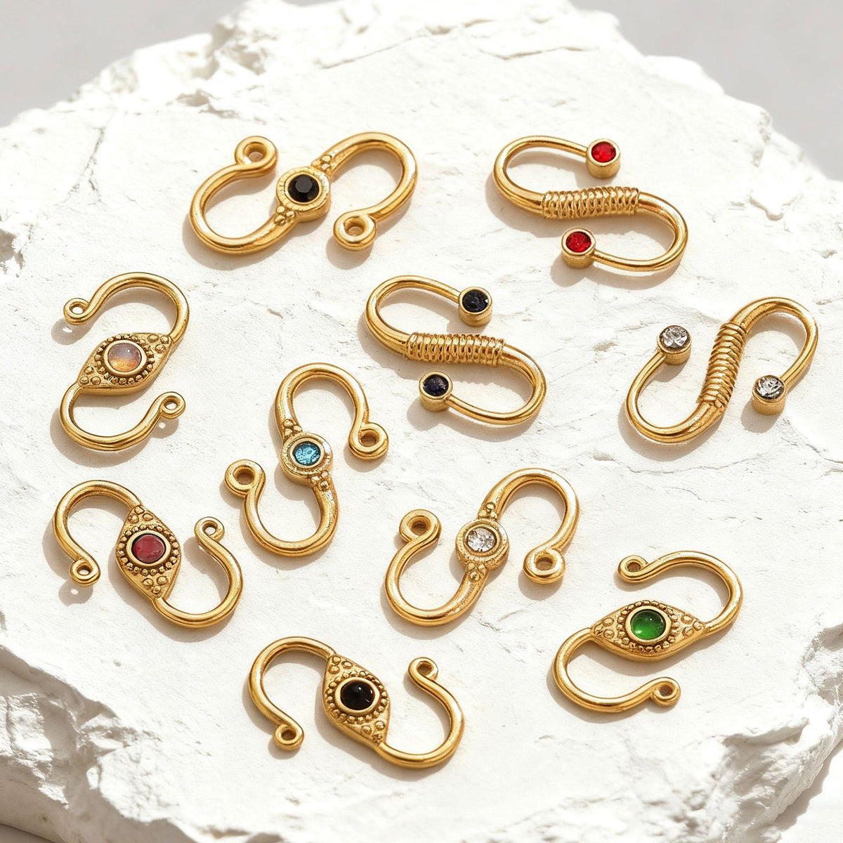 Nine gold stainless steel S-hook jewelry clasps with colorful gemstone inlays on white stone