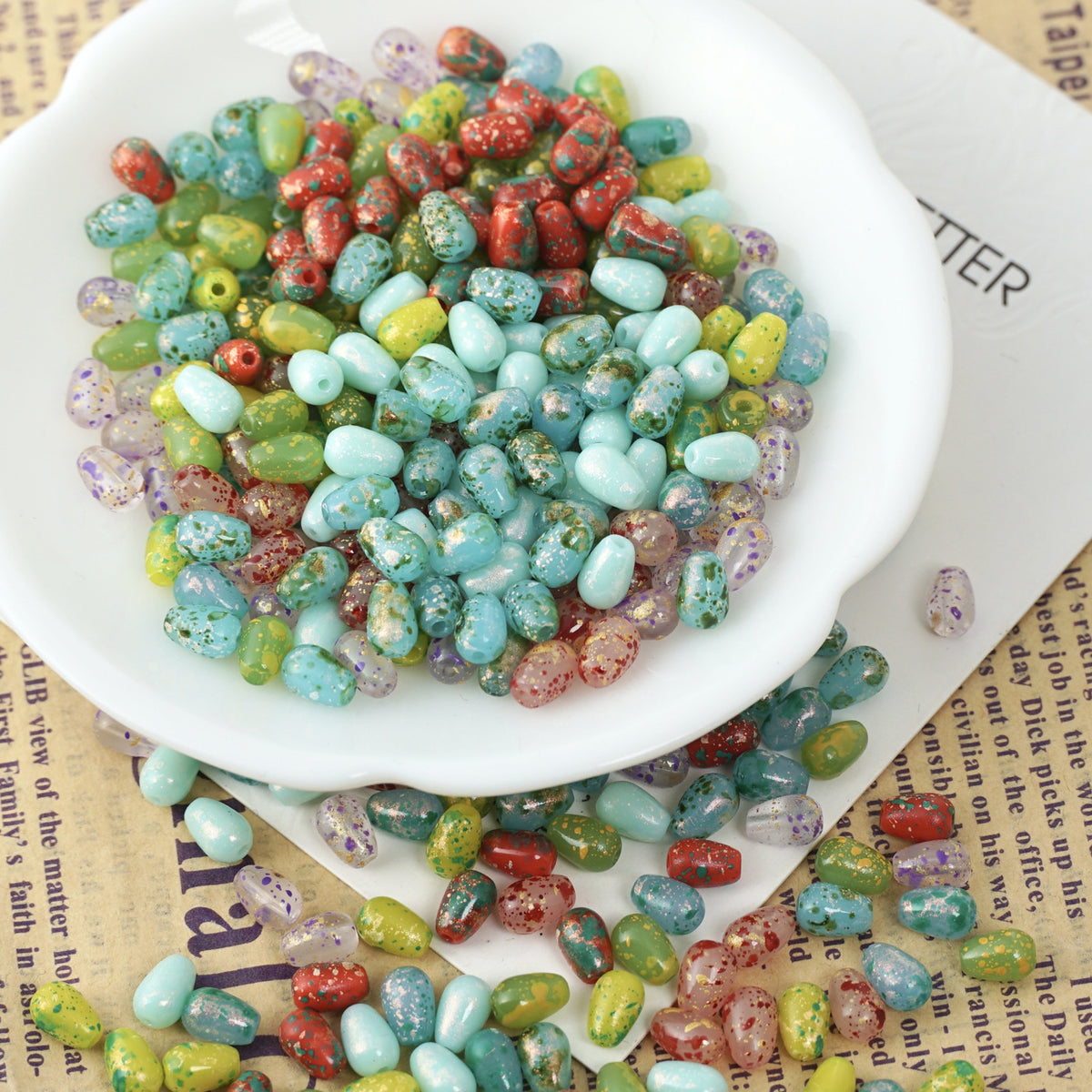 Colorful speckled 4x6mm glass teardrop beads in a white ceramic bowl on newspaper