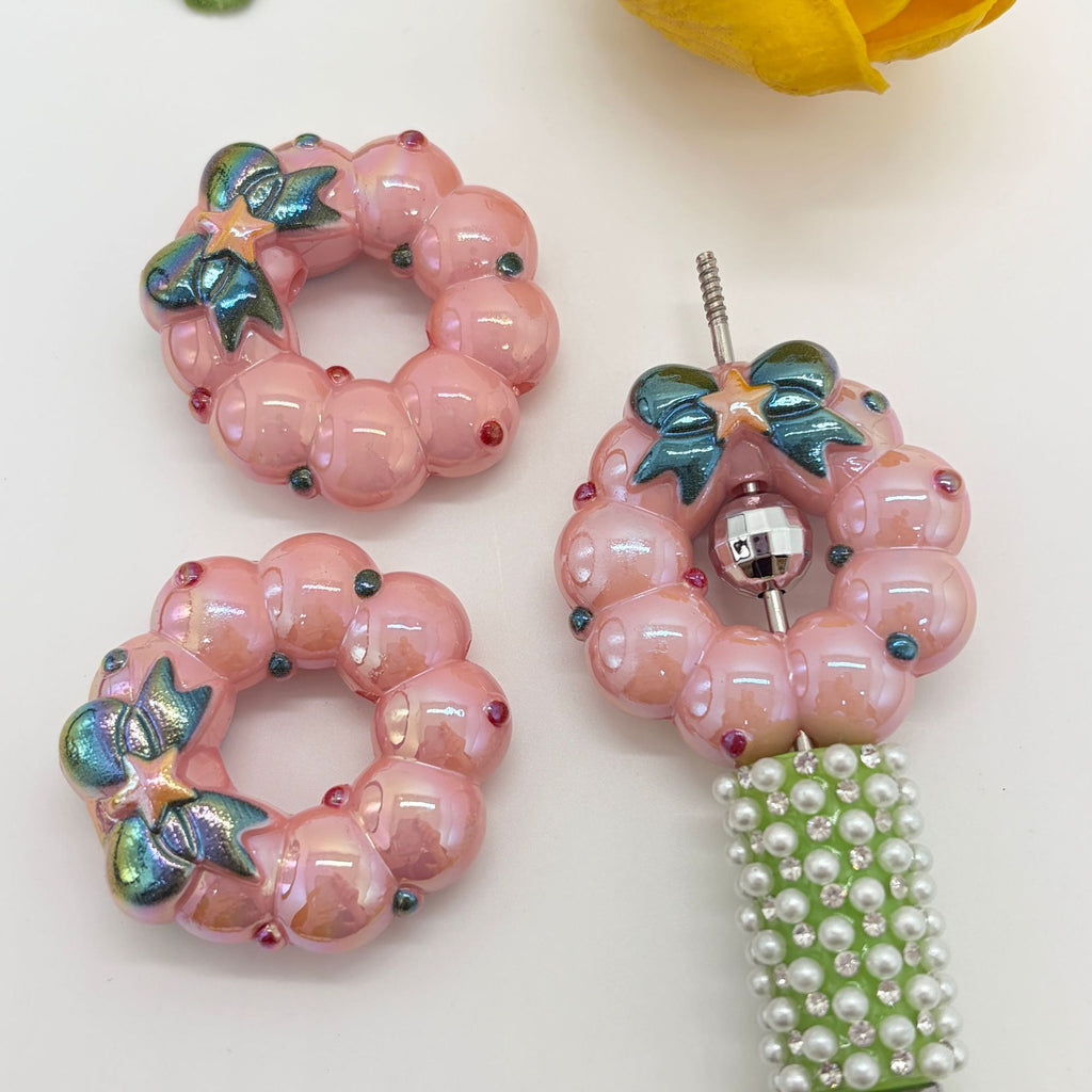Three pink wreath-shaped acrylic focal beads on a white background, including two flat circular beads