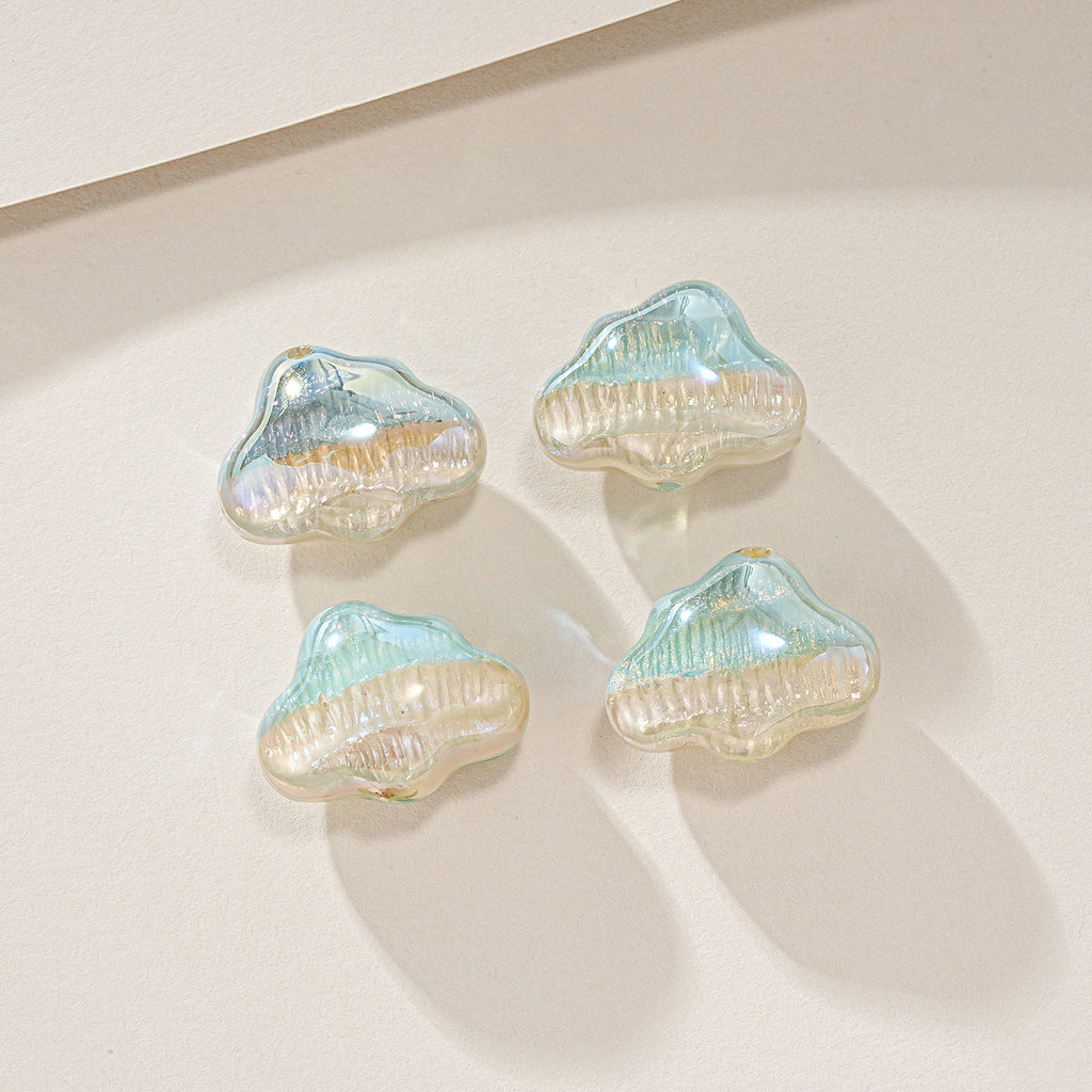 Four cloud-shaped iridescent resin beads with ribbed texture in pale blue and gold on warm beige.