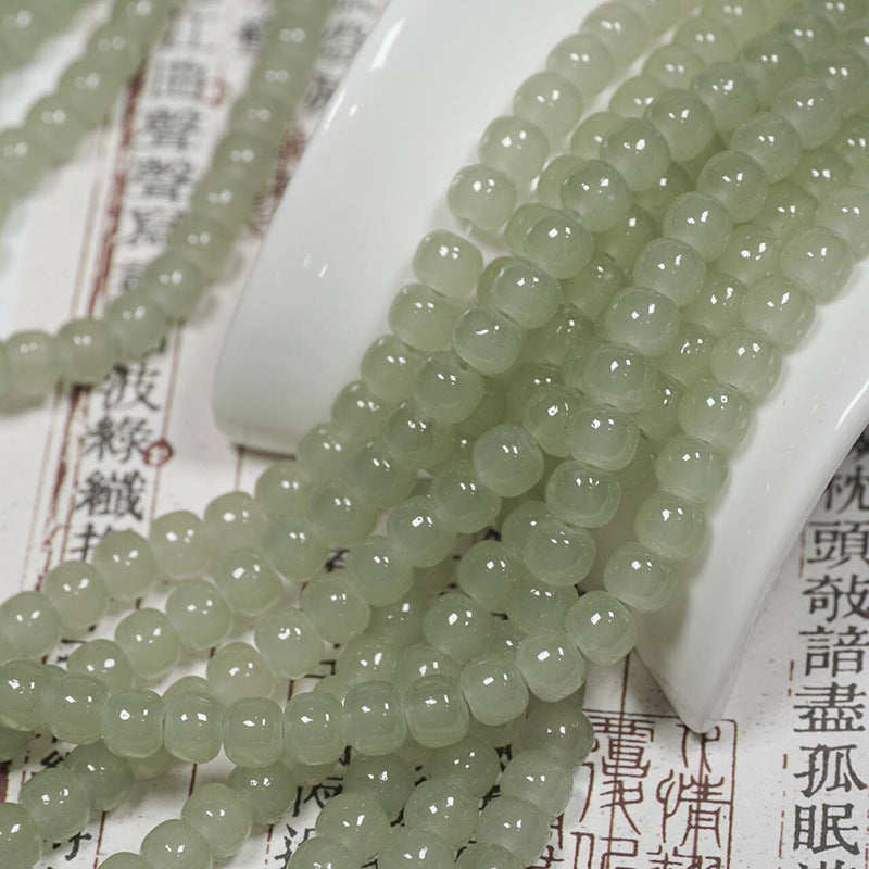Light green translucent drum bead strands over a white ceramic spoon on printed paper with Chinese characters