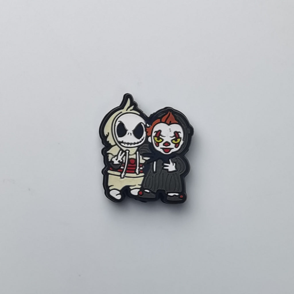 A small cartoon enamel pin featuring two horror characters, one resembling Jack Skellington in a white hoodie and the other resembling Pennywise in a black suit, on a light gray background.