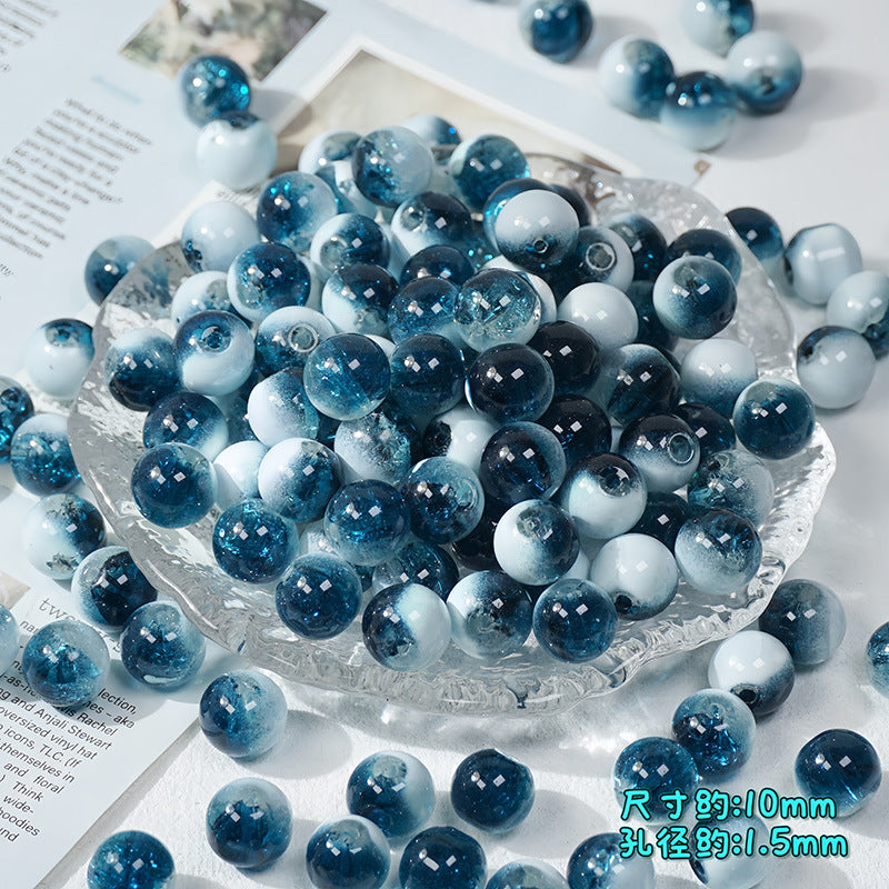 Blue and white ice-crackle glass beads piled in a clear glass dish on a white surface with paper props