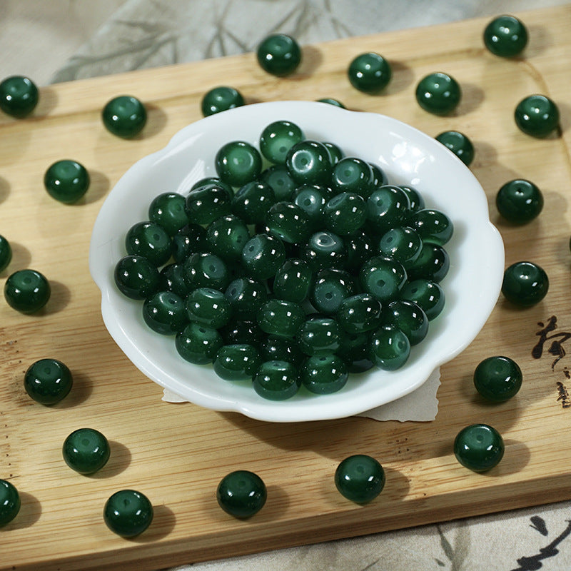 Dark green imitation jade glass beads in a white bowl on a wooden board