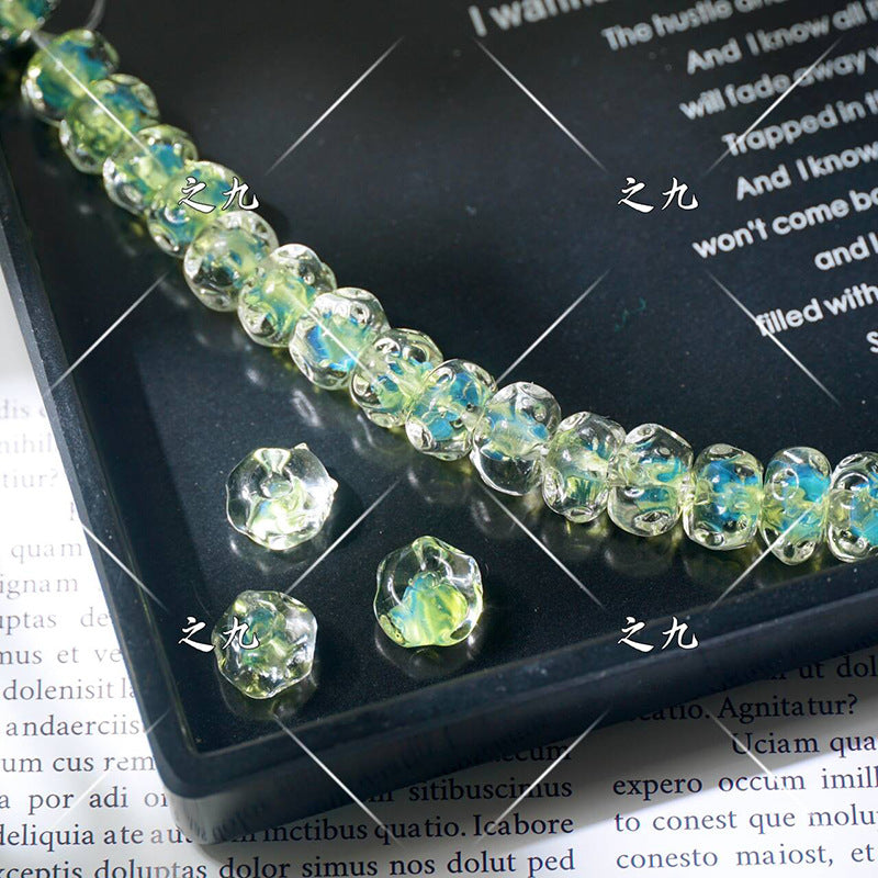 Faceted clear lampwork beads with iridescent green-blue inclusions on a black tray, loose beads