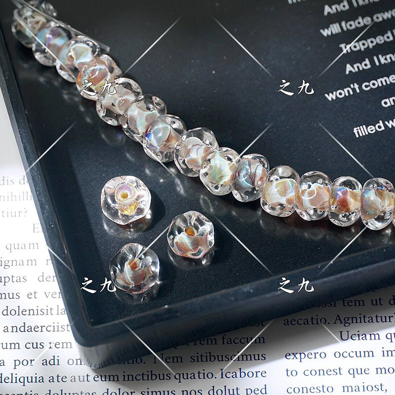 Clear lampwork glass beads with swirled iridescent pattern on a black tray, loose beads