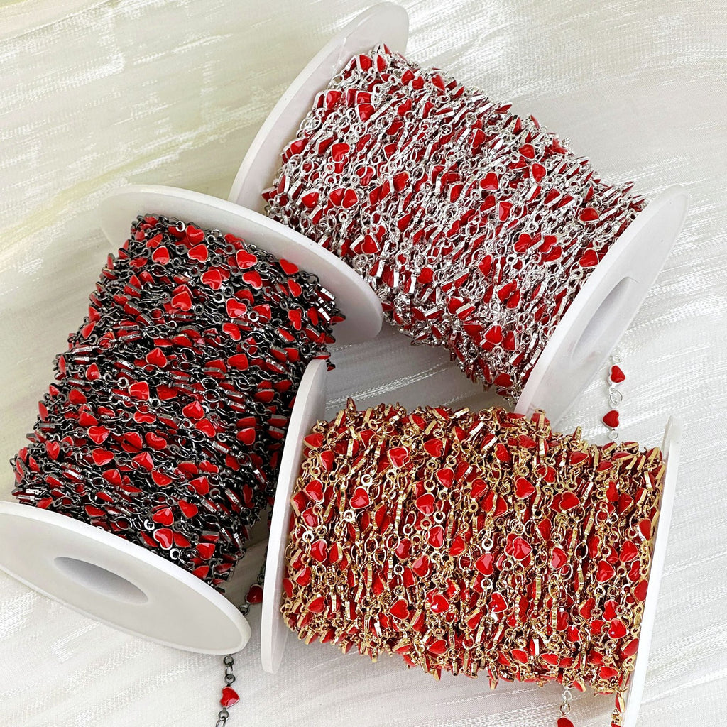 Three spools of red enamel heart station chain in black, silver, and gold metallic tones on white fabric