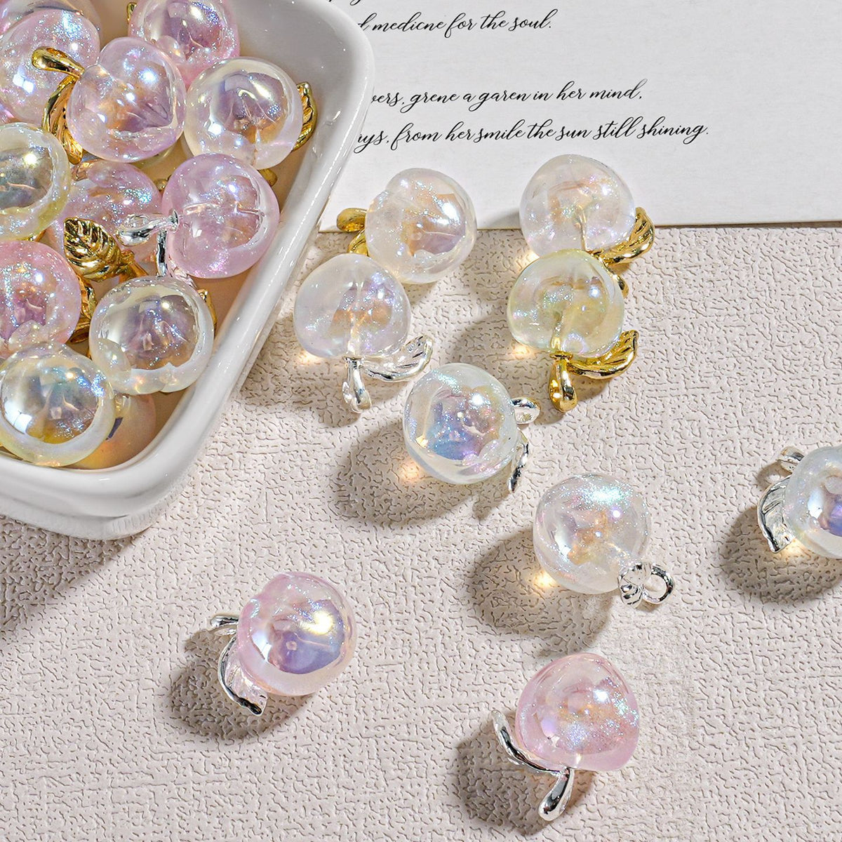 Color-plated alloy mini peach beads with gold and silver leaf accents on a textured beige surface