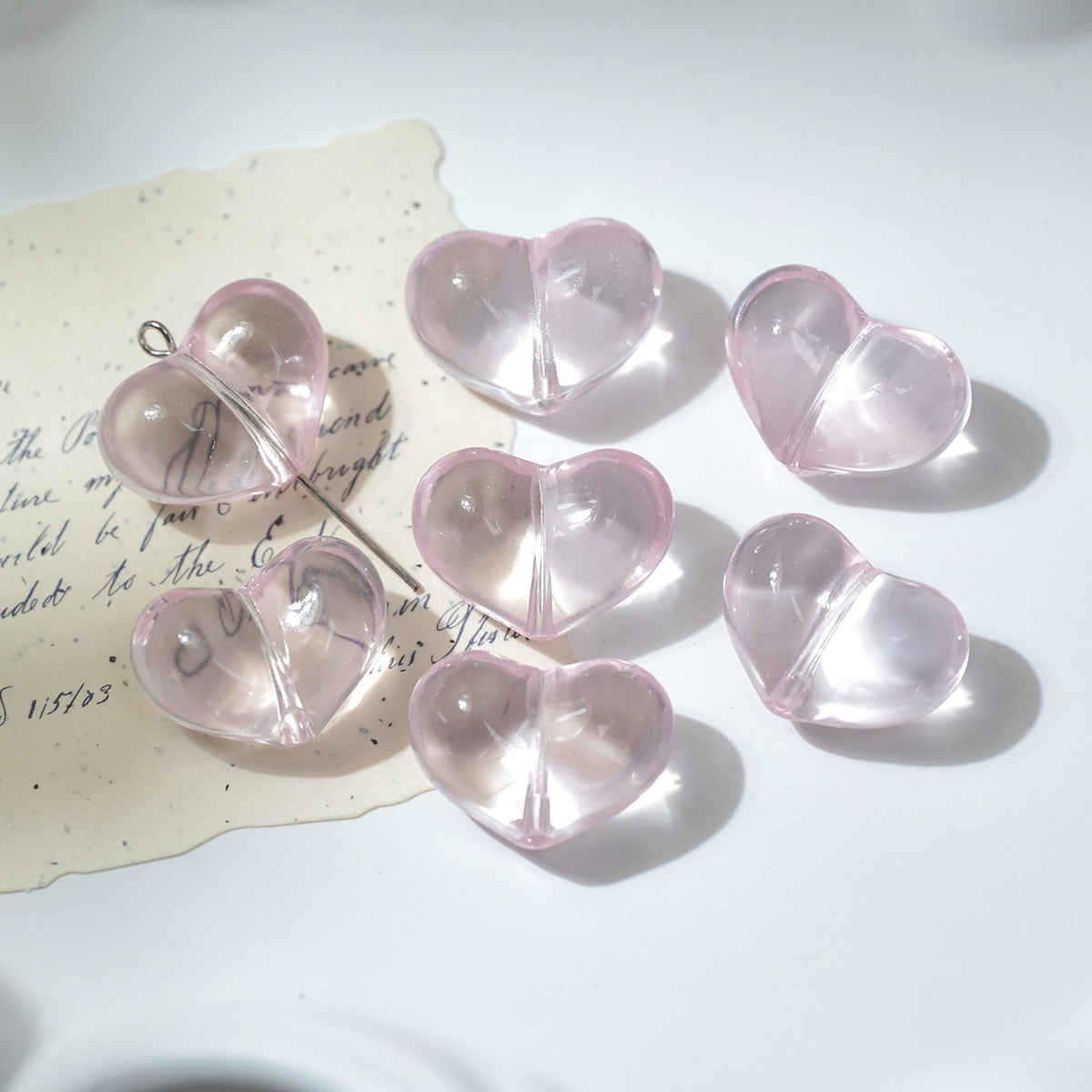 Six translucent light pink heart-shaped glass beads on a white surface