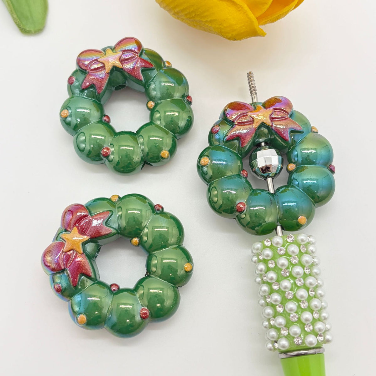 Three green wreath-shaped acrylic focal beads with pink bow details and colorful bead accents