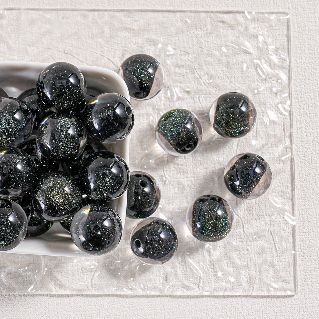 Black glitter round beads in a white dish and scattered on textured white surface