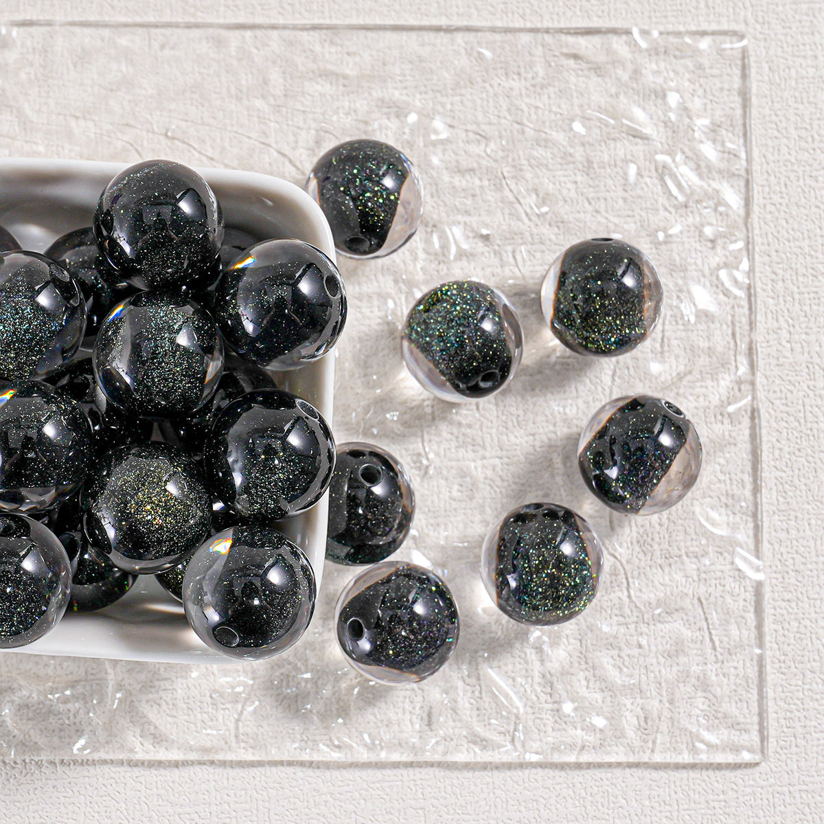 Black glitter round beads in a white dish and scattered on textured white surface
