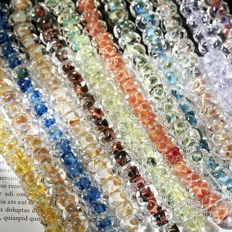 Strands of translucent water-ripple lampwork glass beads in rainbow colors arranged diagonally on printed book pages